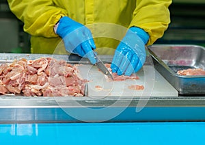 Hand of worker cut and trim chicken meat on cutting board