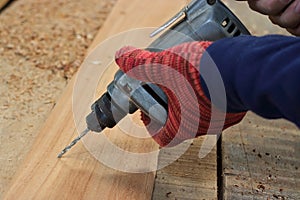 Hand of worker drills a hole with wooden plank using electric drill machine in workshop