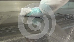 Hand of worker in glove cleans refrigerator display case at supermarket.