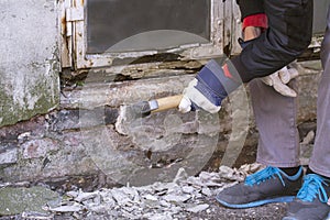 Hand of worker with gloves hammering down plaster on facade that crumbles due to moisture and mold underneath a white wooden frame