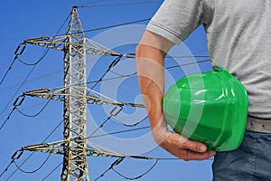 Hand of worker with green hard hat on High voltage electric poles on blue sky background. High voltage electric poles