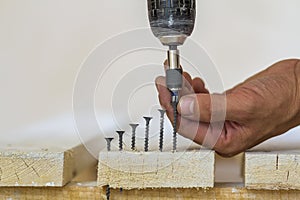 Hand of a worker screws a in a wooden board with a cordles