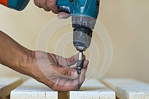 Hand of a worker screws a in a wooden board with a cordles