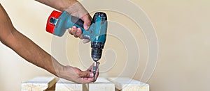 Hand of a worker screws a in a wooden board with a cordles