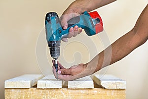 Hand of a worker screws a in a wooden board with a cordles