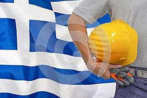 Hand of worker and yellow hard-hat on background flag of Greece