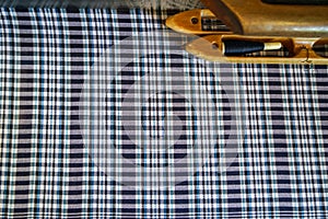 Hand woven cotton fabric in shades of dyed blue and white plaid pattern background with wooden thread shuttle on traditional loom