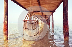 Hand woven natural fiber hammock under a pier, selective focus, color toning applied