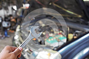 Hand with wrench checking car engine .