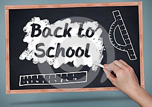 Hand writing back to school on blackboard with chalk and rulers