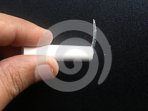 Hand writing on blackboard by white chalk stick