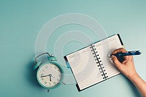 Hand writing on a dairy notebook with an alarm clock