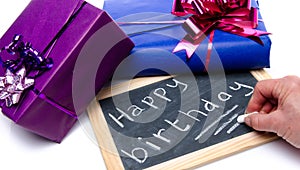 Hand writing happy birthday on a slate blackboard with gifts