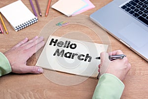 Hand writing Hello March. Office desk with a laptop and stationery