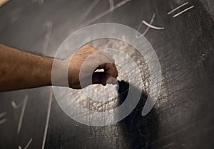 Hand writing maths equations with chalk on a blackboard. Perspective from below