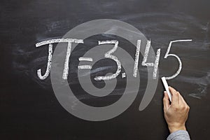 Hand writing the number Pi on a chalkboard