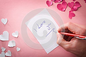 Hand writing romantic note on pink background with hearts