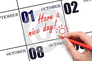 The hand writing the text Have a nice day and drawing the sun on the calendar date October 1