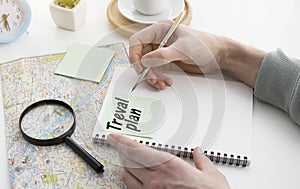 Hand writing travel plan in a lined spiral notepad arranged on a map