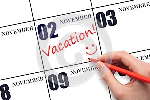 A hand writing a VACATION text and drawing a smiling face on a calendar date 2 November. Vacation planning concept.