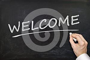 Hand is writing Welcome word on blackboard. Invitation concept