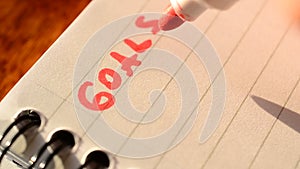 Hand writing the word GOALS with red marker in notepad