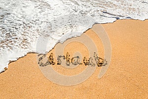 Hand written text in German Urlaub English translation holidays on the golden beach sand with coming wave
