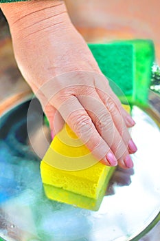 hand with yellow antibacterial sponge clean metallic surface