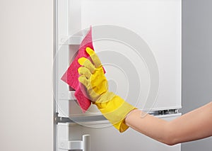 Hand in yellow glove cleaning white refrigerator with pink rag