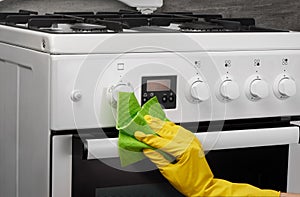 Hand in yellow glove cleaning white stove with green rag