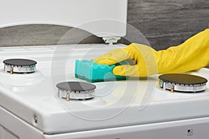 Hand in yellow glove cleaning white stove with green sponge