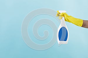 Hand in yellow glove holds spray bottle of liquid detergent on blue background. cleaning