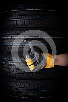 Hand in yellow gloves and car tires on black background, closeup.