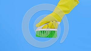 A hand in yellow gloves showing a green brush against blue background, cleaning and brushing carpet, removing stains and wool from