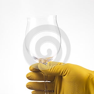 A hand in a yellow latex glove holds a glass goblet on a white background