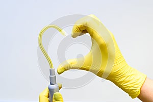 Hand in yellow latex glove and saliva ejector in shape of heart on a white background