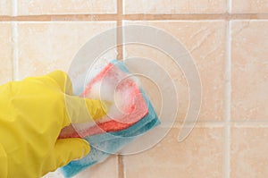Hand in yellow protective glove with sponge washes ceramic tiles with washing foam . Early spring cleaning or regular