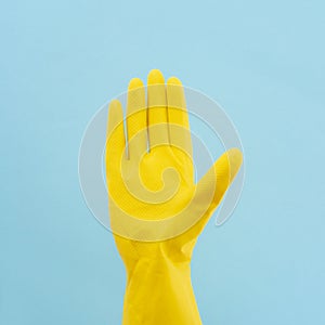 Hand in yellow rubber glove on blue background. Protective latex gloves. Minimal creative cleaning service concept