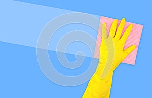 Hand in a yellow rubber glove with a pink cleaning sponge leaves a stripe on a blue background with a copy space