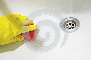Hand in yellow rubber glove with sponge wash sink