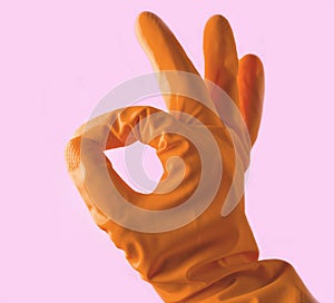 Hand in yellow rubber gloves shows thumbs symbol okay on pink