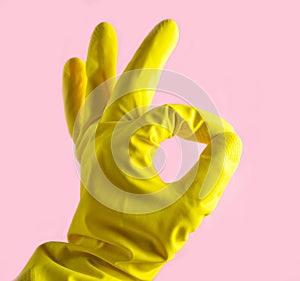 Hand in yellow rubber gloves shows thumbs symbol okay on pink background