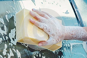 Hand with yellow sponge and soap are washing a car
