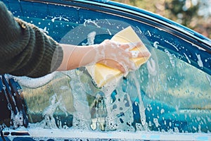 Hand with yellow sponge and soap are washing a car