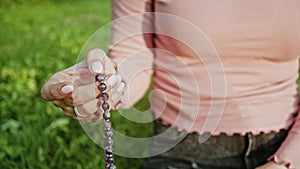 Hand of young believing woman prays in nature and uses craft rosary beads to count prayer and concentrate on meditation