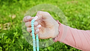 Hand of young believing woman prays in nature and uses craft rosary beads to count prayer and concentrate on meditation