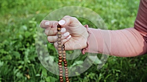 Hand of young believing woman prays in nature and uses craft rosary beads to count prayer and concentrate on meditation