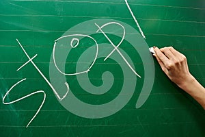 Hand of a young girl writing the word STOP on the green school board