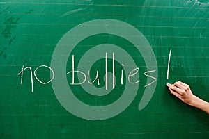 Hand of a young girl writing the words NO BULLIES on the green school board
