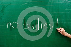 Hand of a young girl writing the words NO BULLIES on the green school board photo